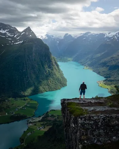 Randonneur debout au sommet de Klovane contemplant le lac Oldevatnet aux eaux turquoise, entouré de montagnes et de glaciers dans la région d'Olden, en Norvège.