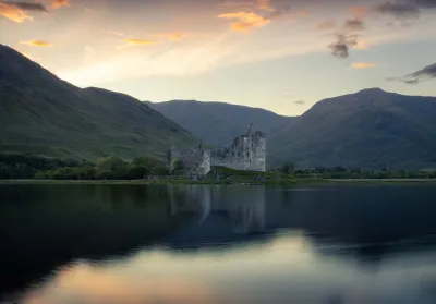 Ruines du château de Kilchurn sur une presqu'île du Loch Awe, baignées par la lumière dorée du coucher de soleil, avec le lac au premier plan.